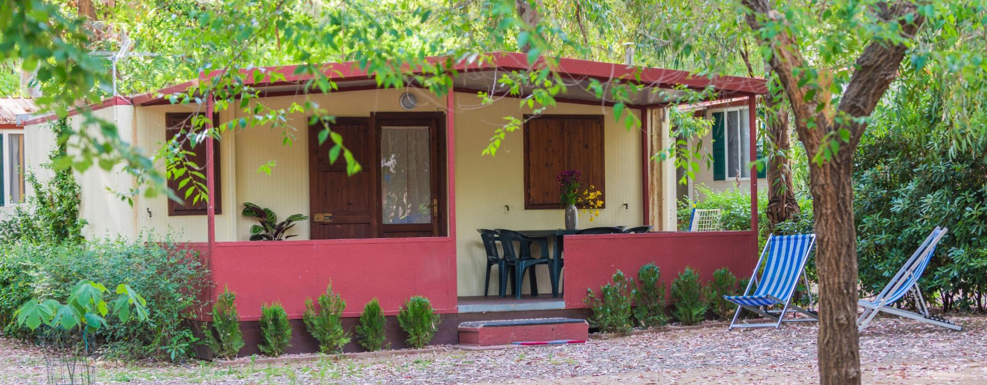 Piccola casa immersa nel verde, con veranda, sedie a sdraio e fiori.