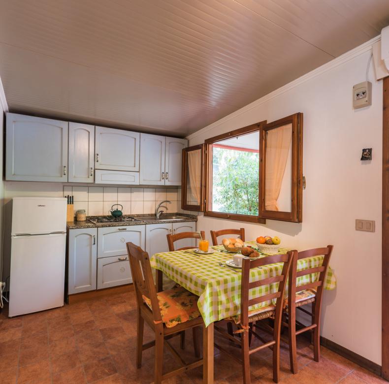 Cucina accogliente con tavolo apparecchiato, finestre aperte e mobili bianchi.