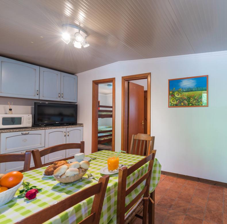 Cucina con tavolo apparecchiato, elettrodomestici e accesso a una stanza con letti a castello.