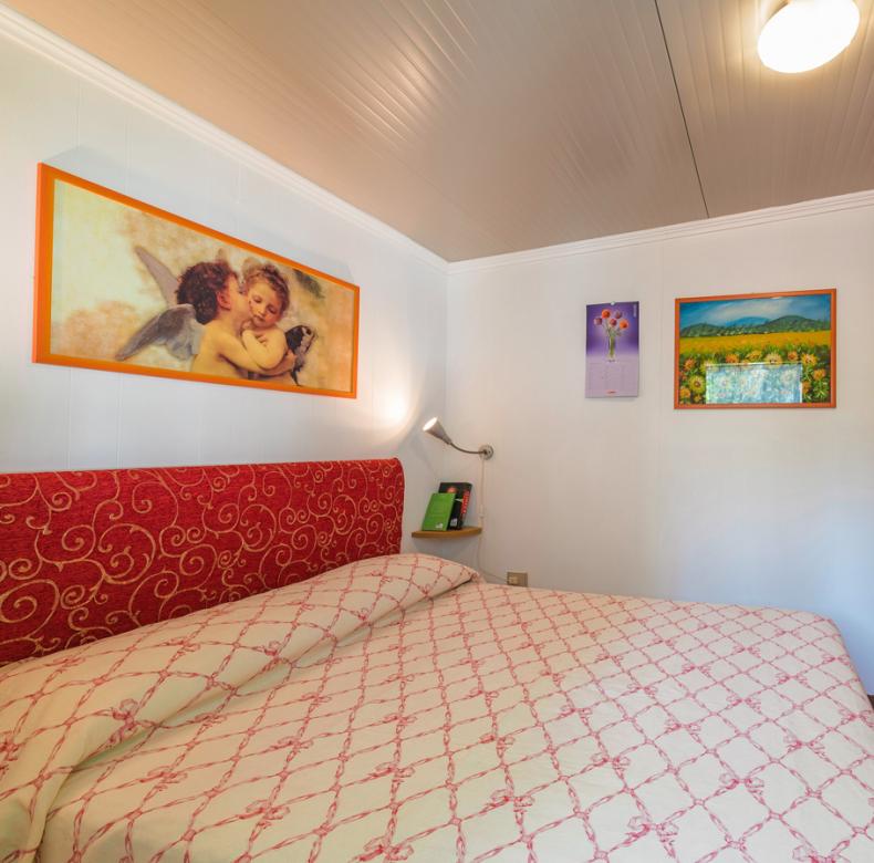 Camera da letto accogliente con letto matrimoniale, armadio in legno e quadri colorati.