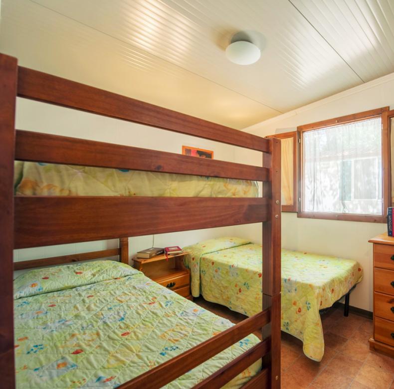Camera con letto a castello, finestra aperta, cassettiera e decorazioni floreali.